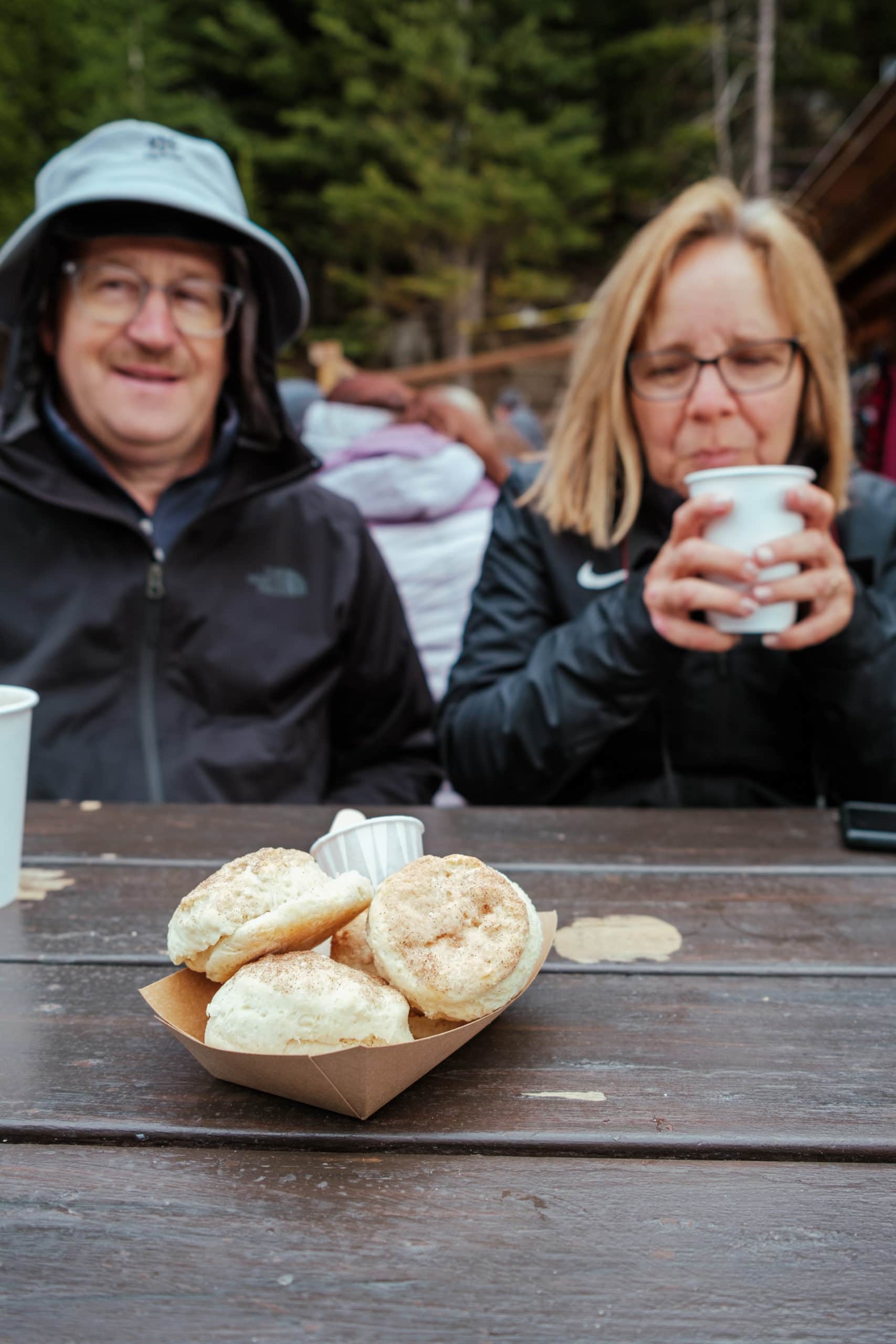 People sitting at a table at the Lake Agnes Tea House, with scones in front of them.