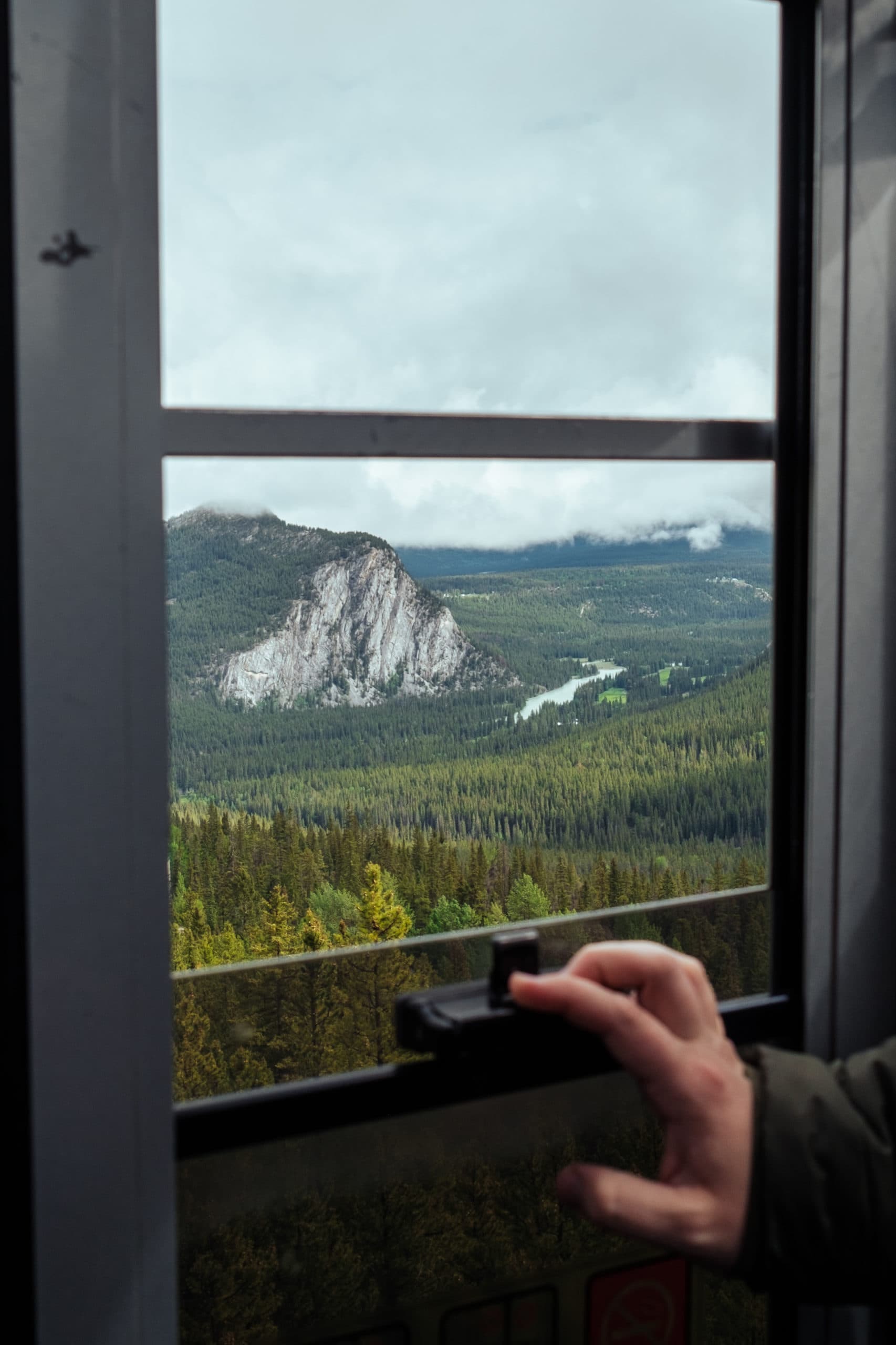 A hand pulls down a window inside the Banff Gondola.