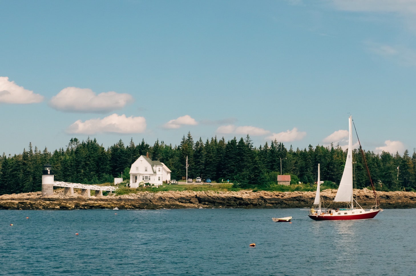 A sailboat floats along beside a lighthouse.