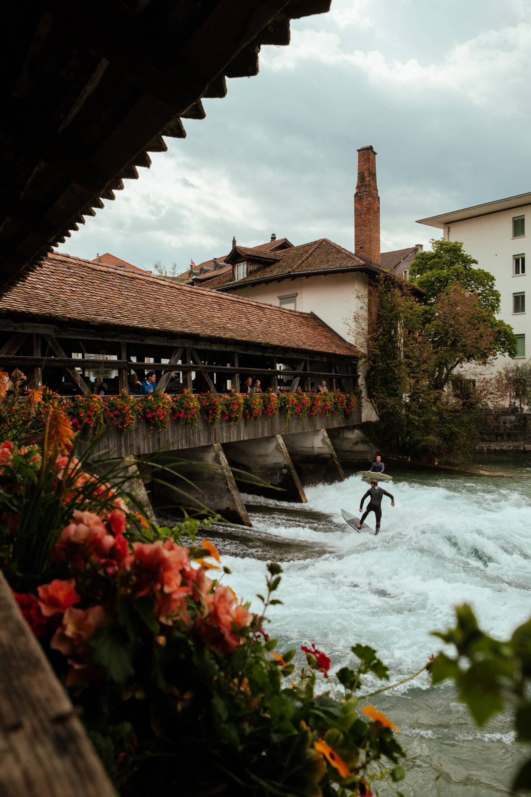People surf below a wooden bridge in Thun.