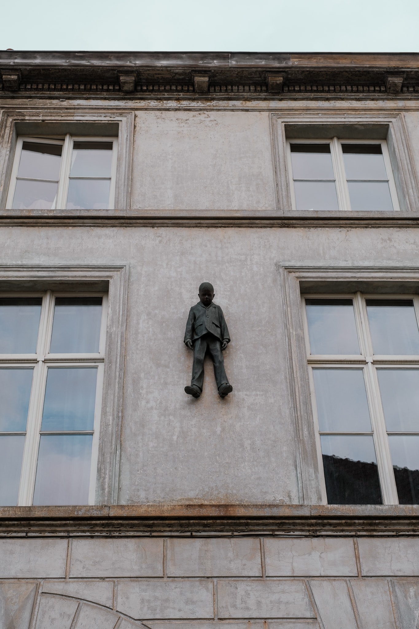 A statute of a boy hangs off a building.