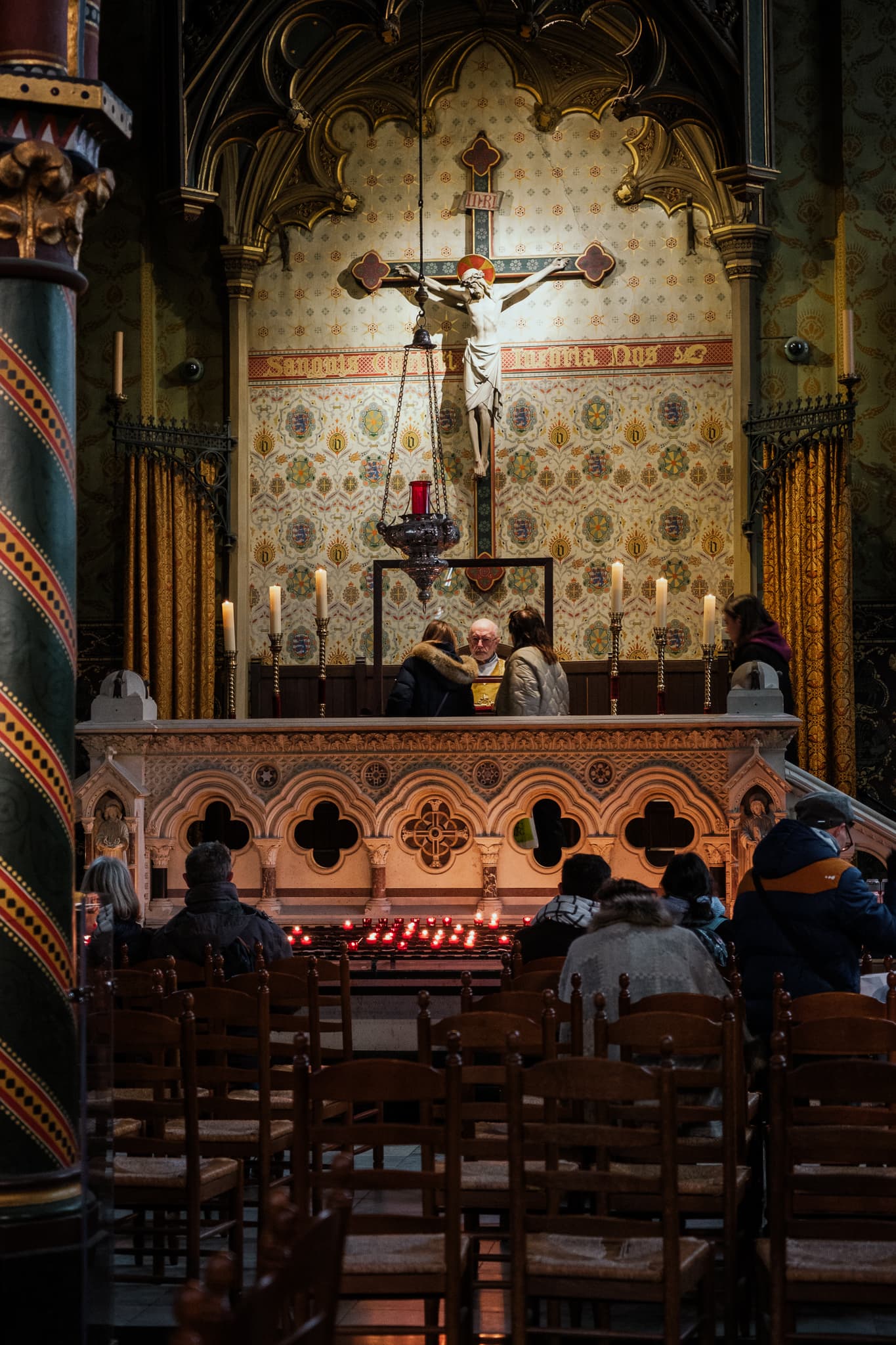 A priest sits inside the Basilica of the Holy Blood, while people look at the relic.
