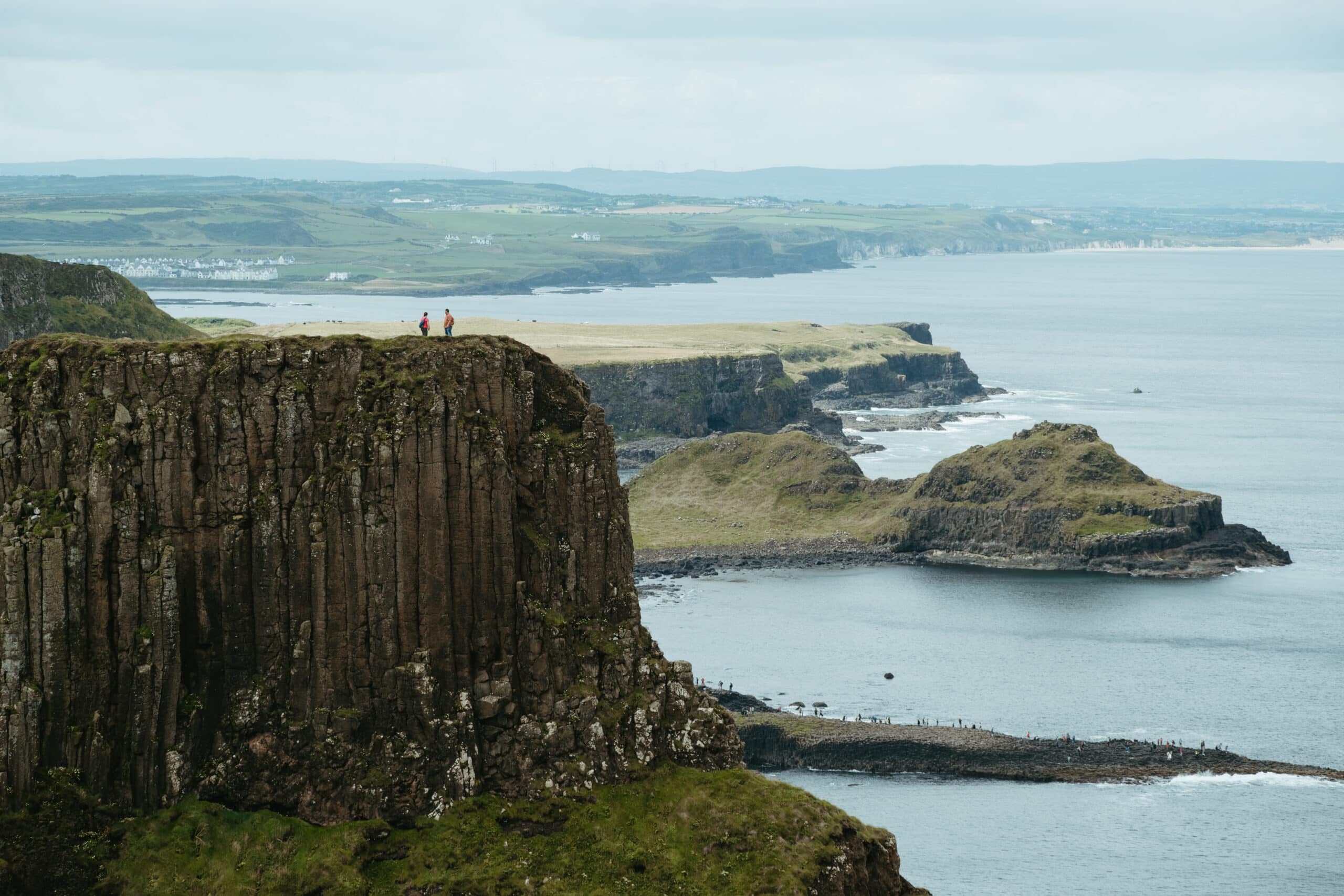 Two people stand at the top of a cliff along the Causeway Coastal Route.