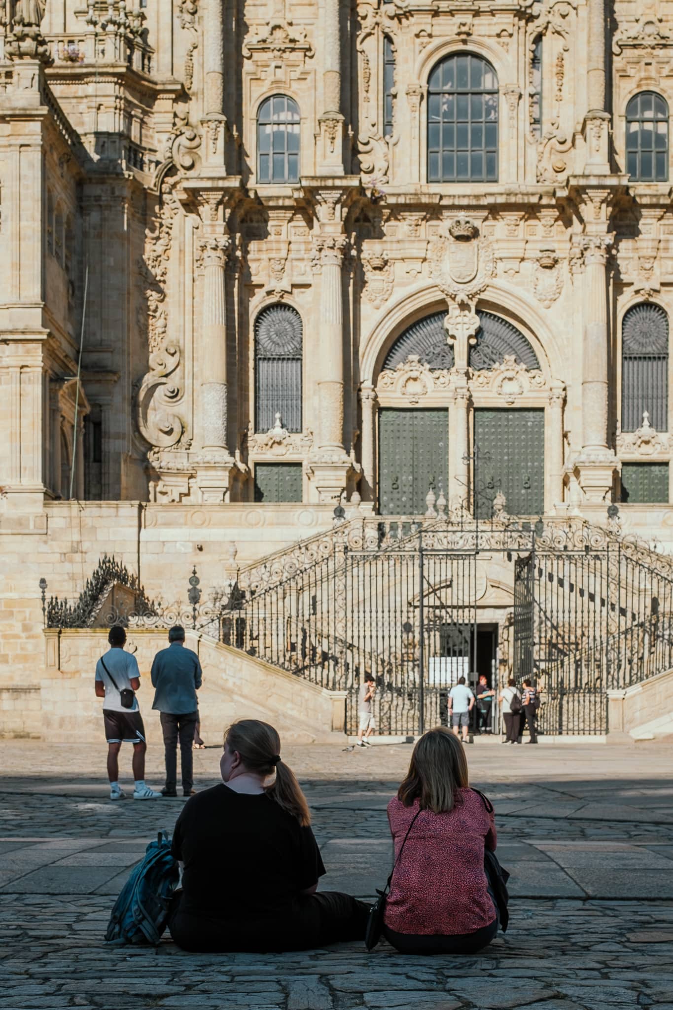 Two women sit in front of the Santiago de Compostela cathedral.