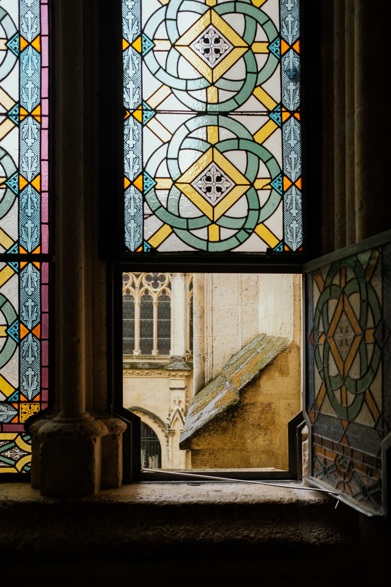 A stained-glass window is partially open, revealing a cathedral wall.
