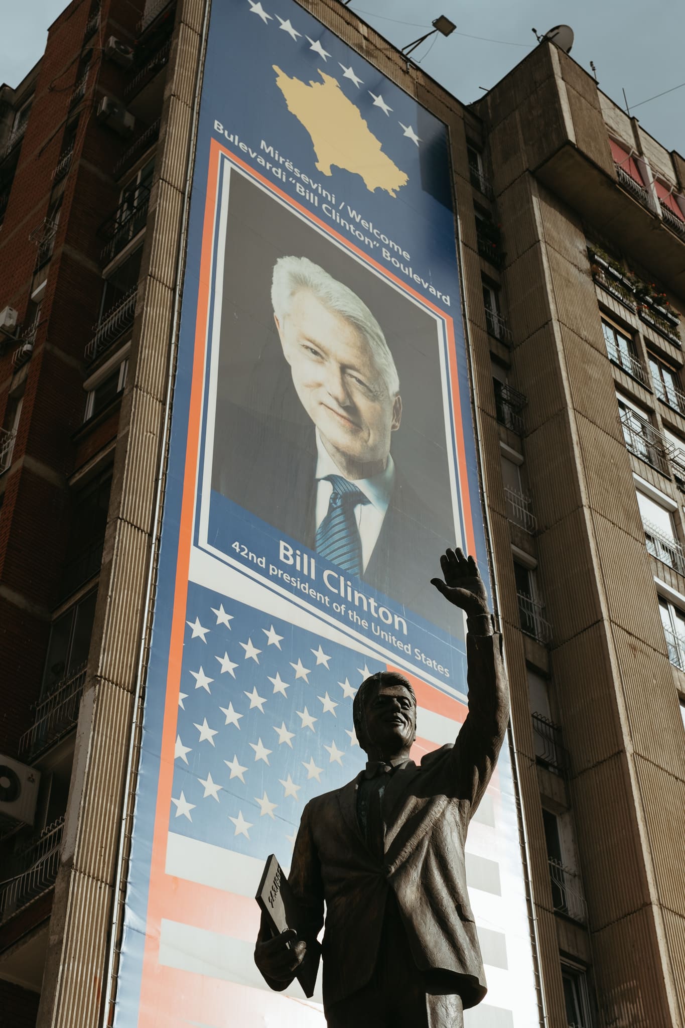 A statue of Bill Clinton in front of a sign about Bill Clinton in Pristina.