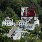 The red and white Laxey Wheel stands amidst green trees.