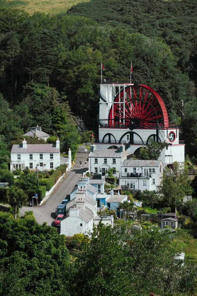 The red and white Laxey Wheel stands amidst green trees.