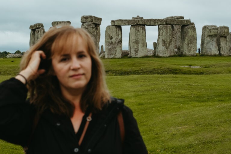 A woman (me!) runs her hand through her hair in front of Stonehenge.