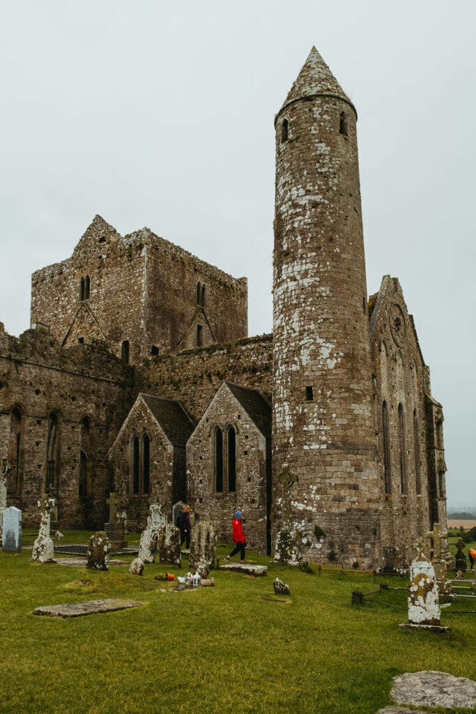 Large stone ruins stand amidst green grass and old graves.