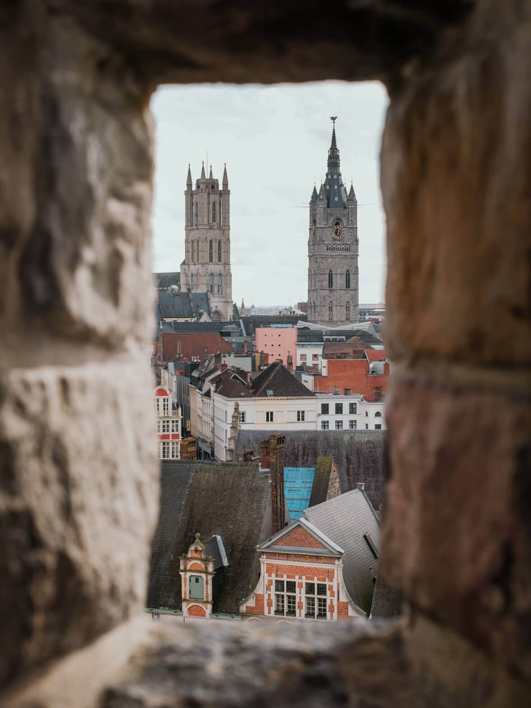 Towers and rooftops of Ghent visible through a castle window.
