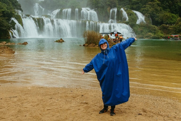 Wearing a huge poncho, I throw out my arms in front of Ban Gioc Waterfall.