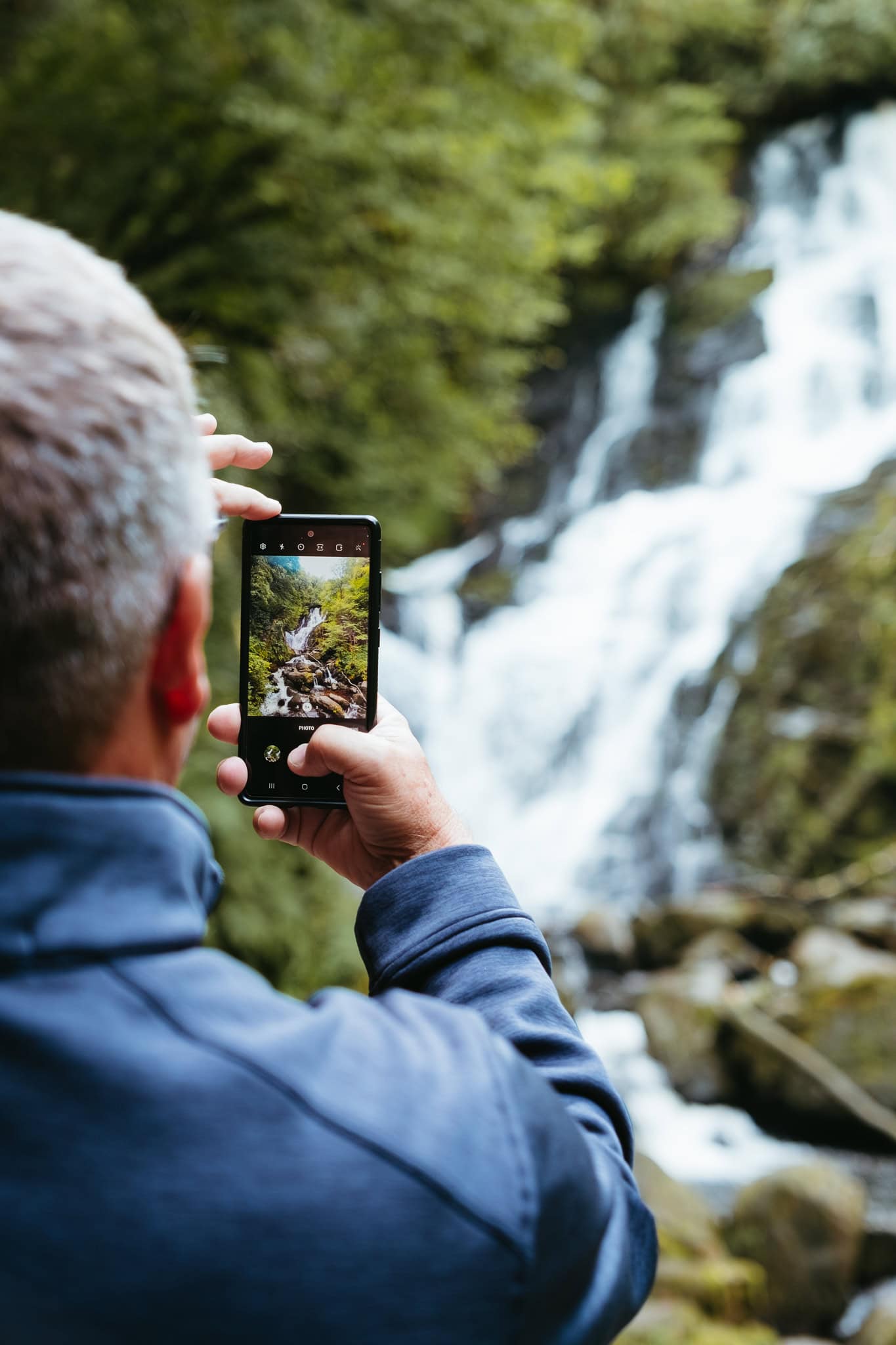 My dad holds up his phone to take a picture of Torc Waterfall.