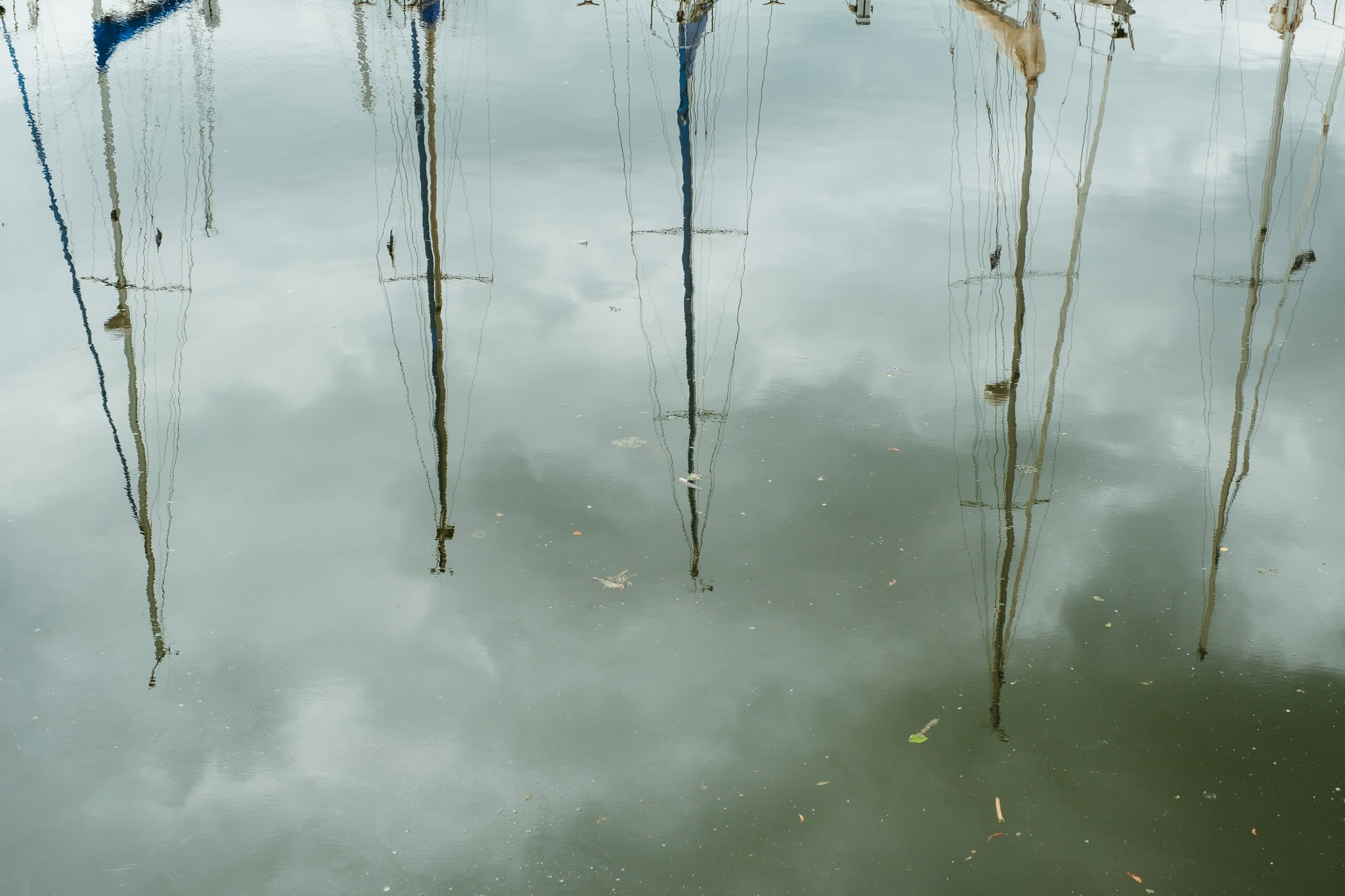Masts of sailboats reflecting in water below.