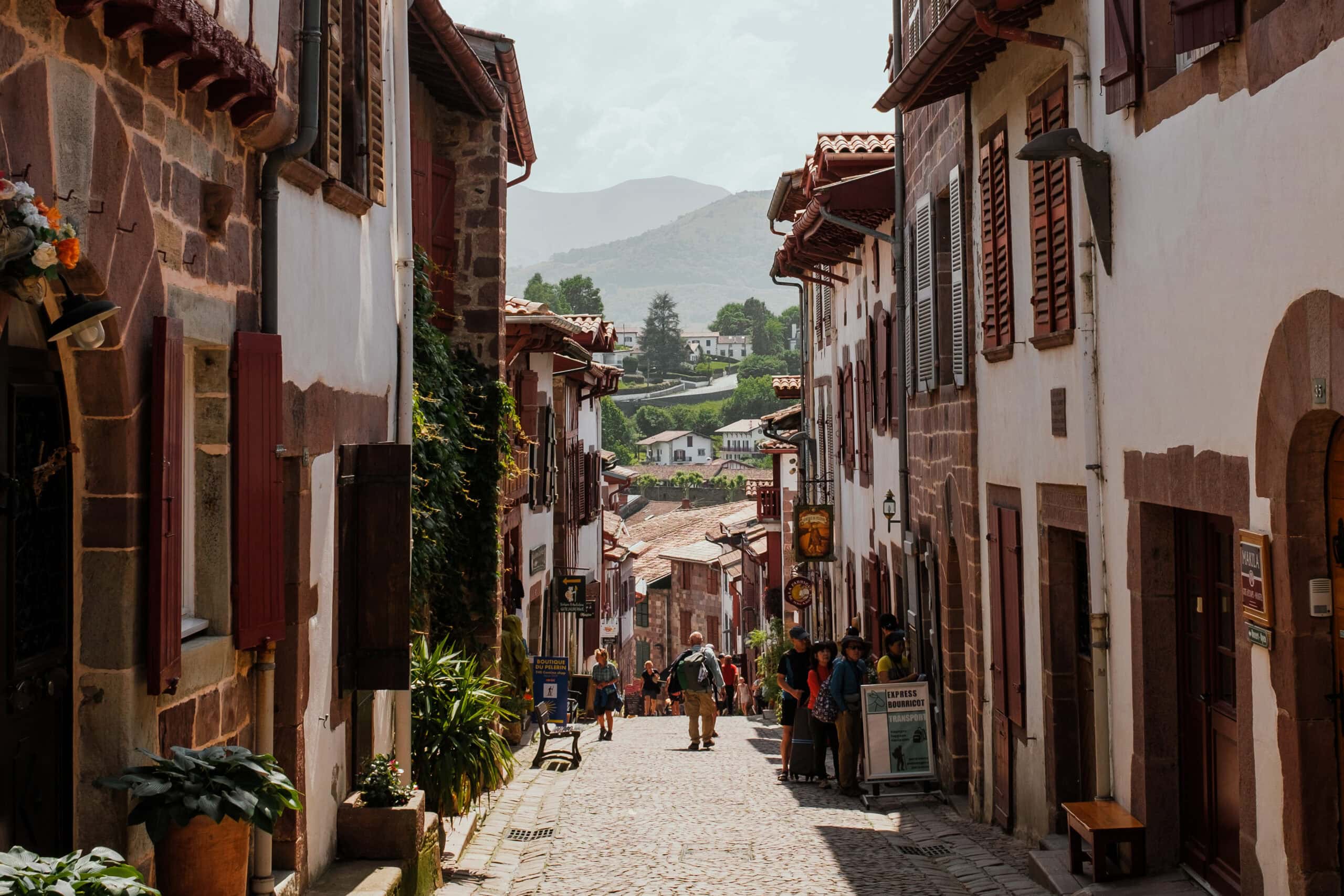People walking down a street in Saint Jean Pied de Port, with mountains visible in the distance.