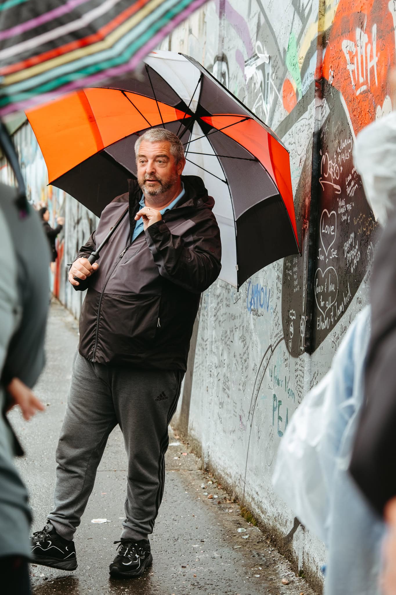 A tour guide carrying an umbrella speaks to a group beside Belfast's peace wall.