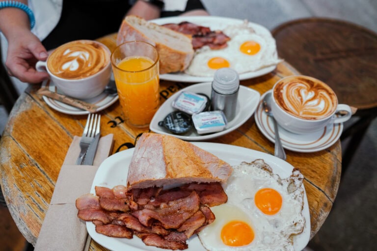 Plates with. ham, eggs, and bread, beside coffee and juice.
