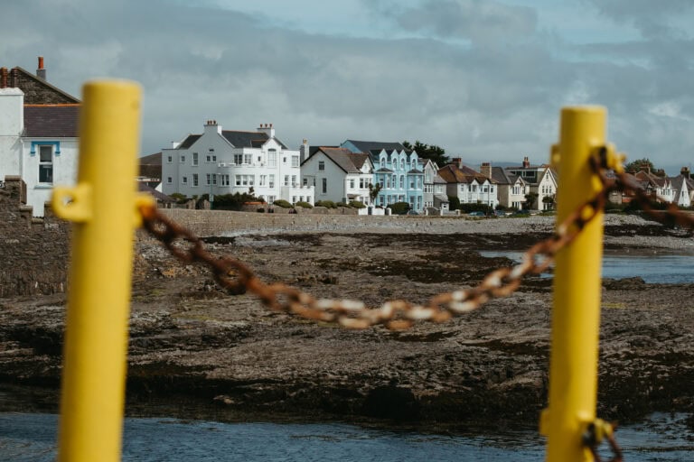 Buildings along the coast behind a chain link on yellow posts.