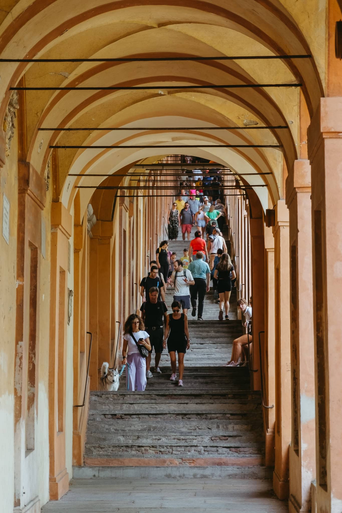 People walking up and down the stairs in the arched Portico di San Luca.