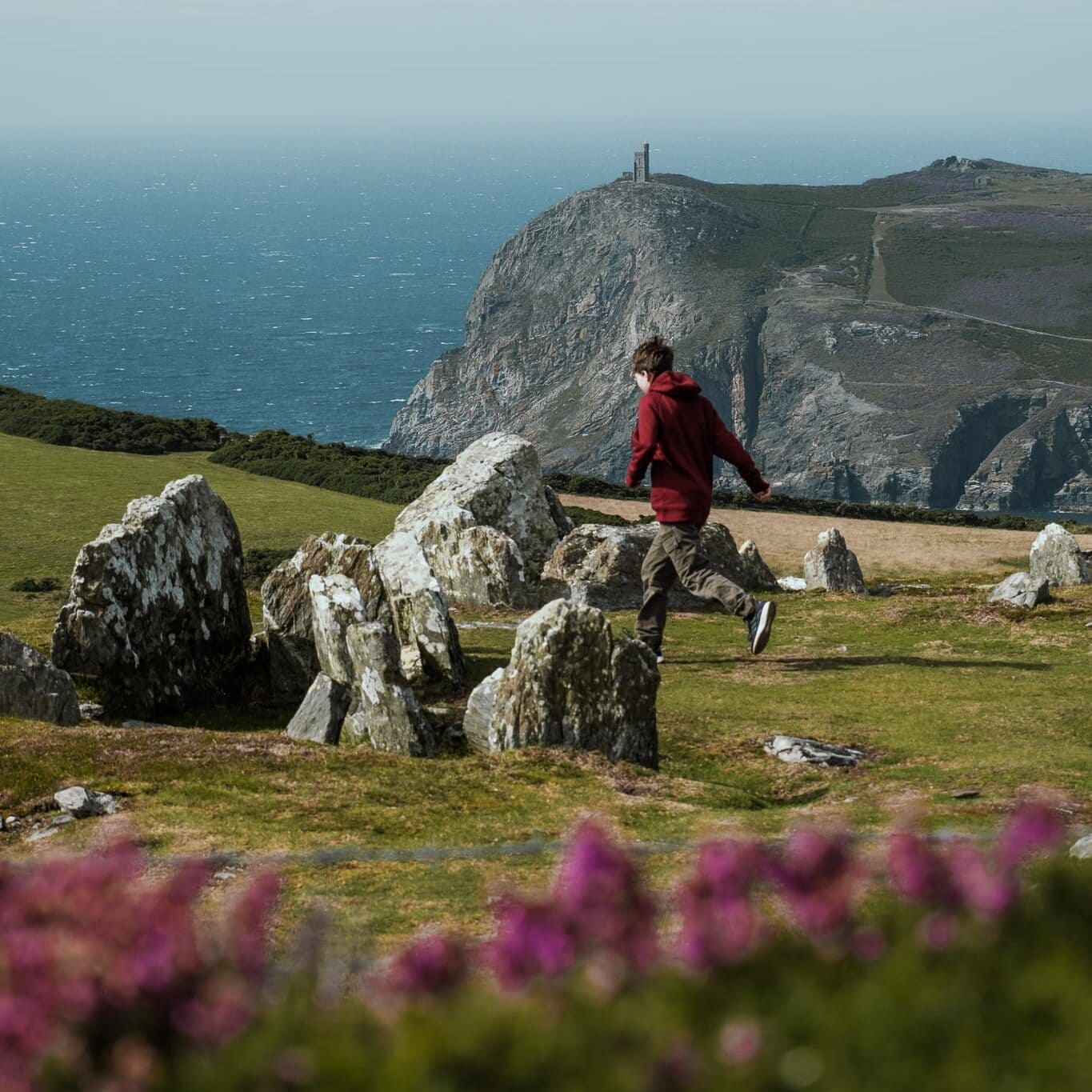 A boy runs through Meayll Circle. In the distance, Milner's Tower stands above the sea.
