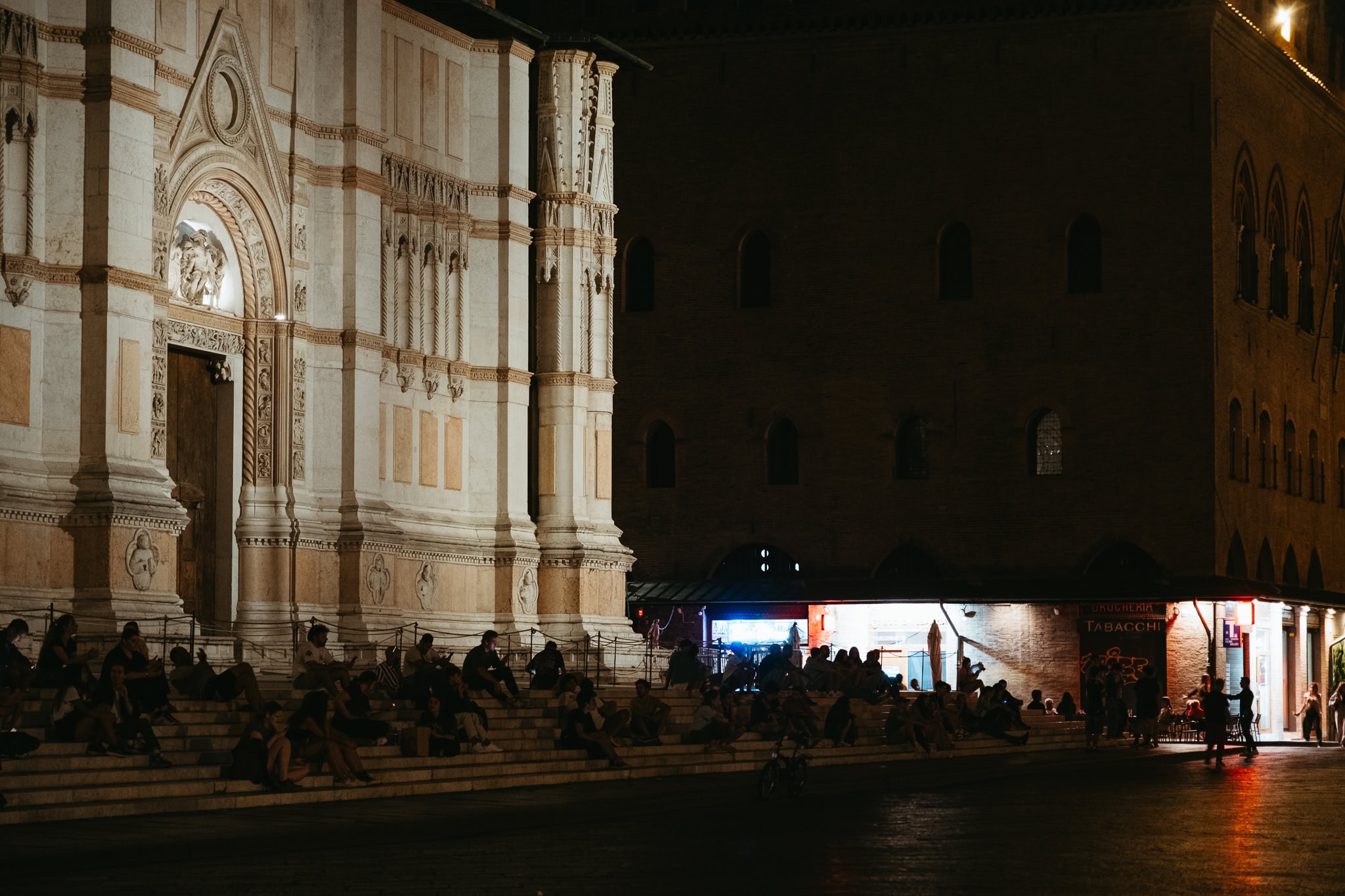 People sit on the front steps of the Bologna Cathedral at night.