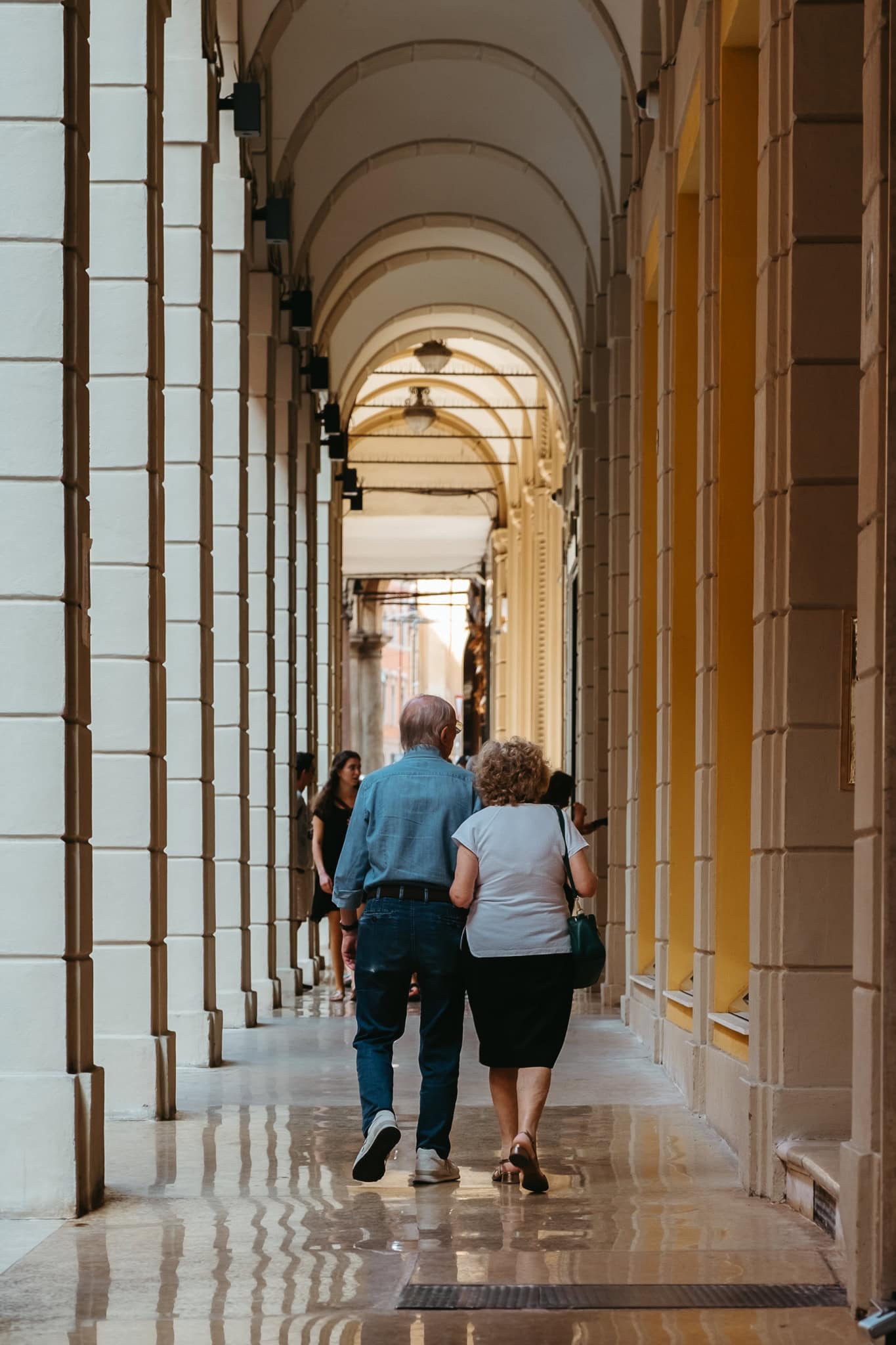 A couple walks under a Bologna portico.