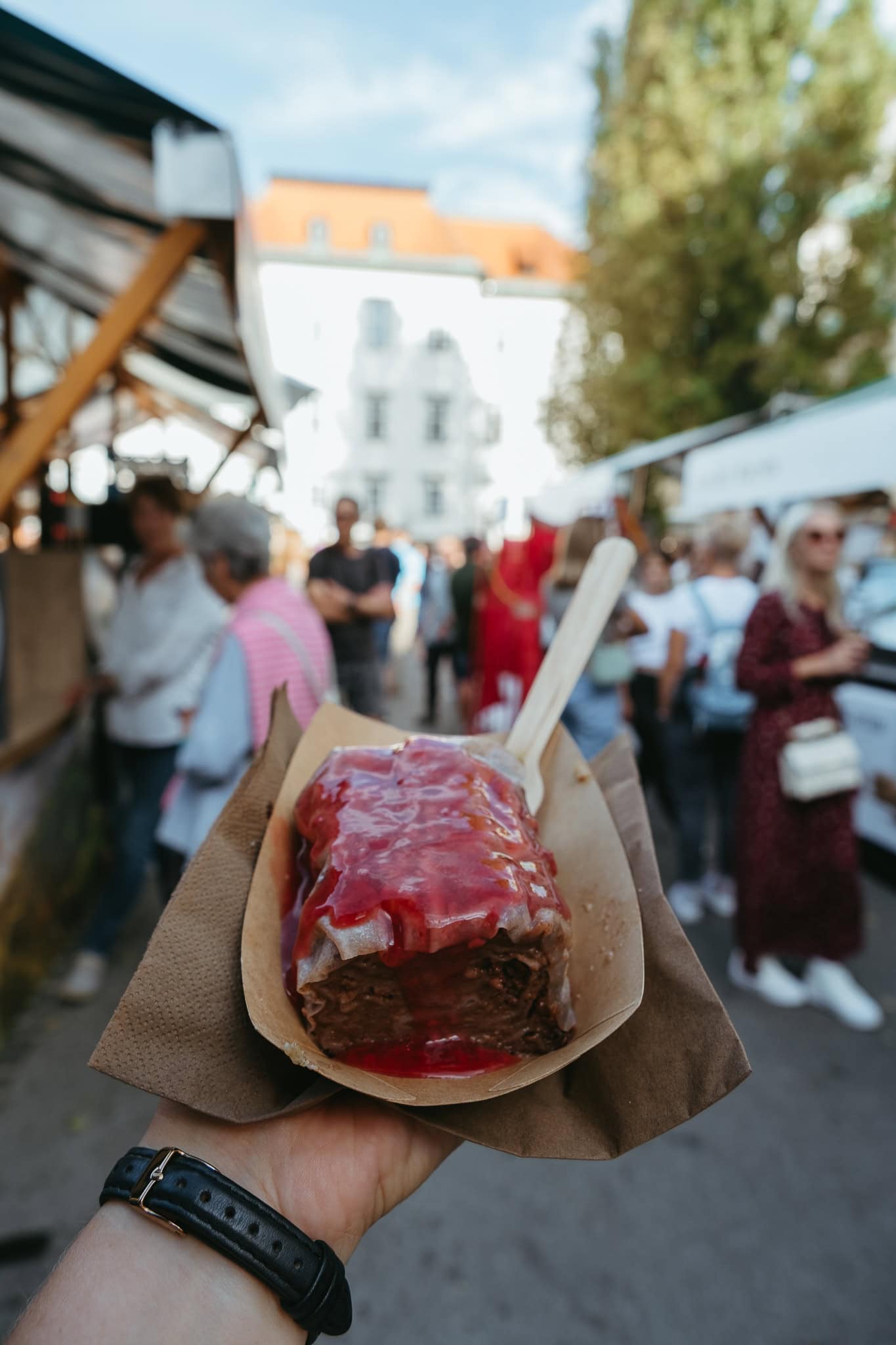 A hand holding out a Slovenian dumpling, covered in red sauce.