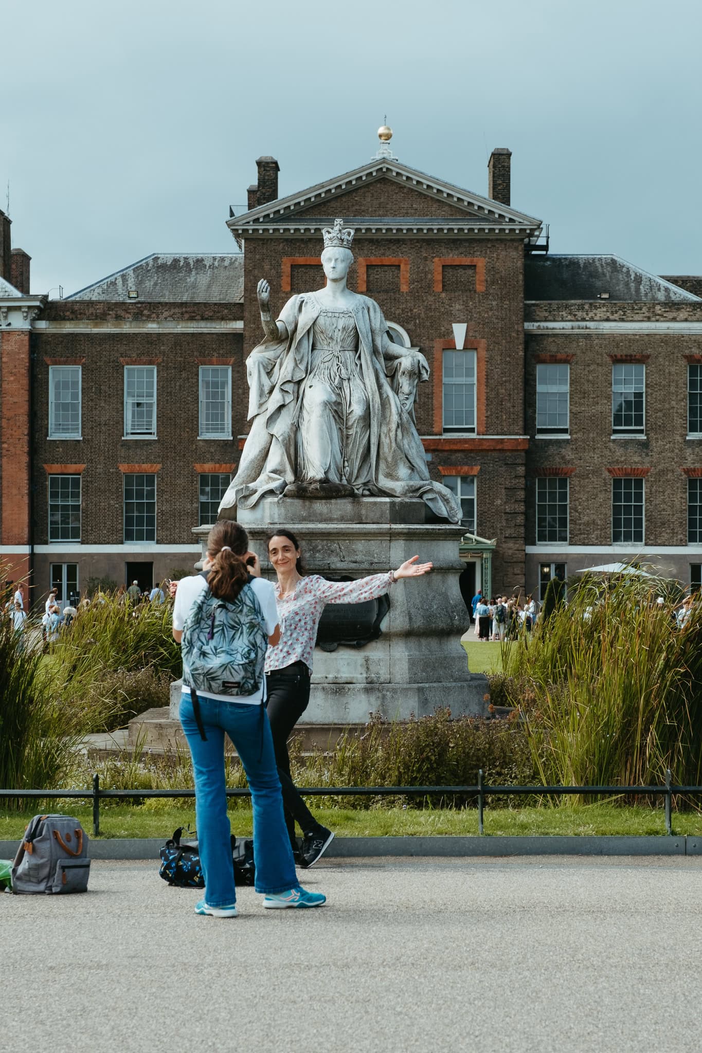 A woman poses in front of a statue of Queen Victoria, which sits in front of Kensington Palace.