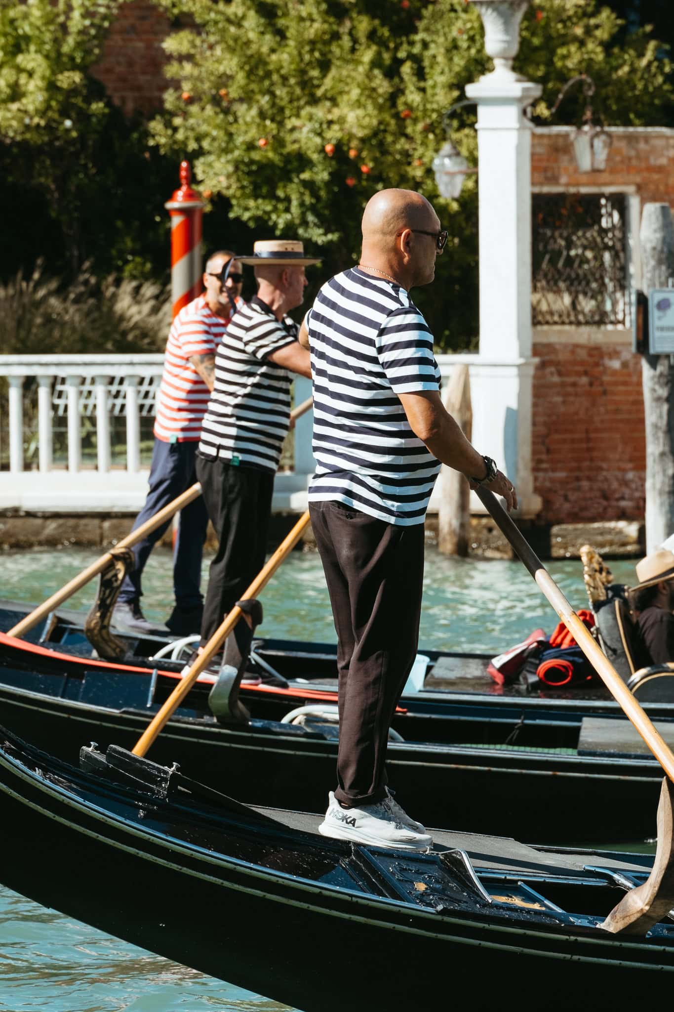 Three gondoliers in striped shirts standing on boats in the Grand Canal.