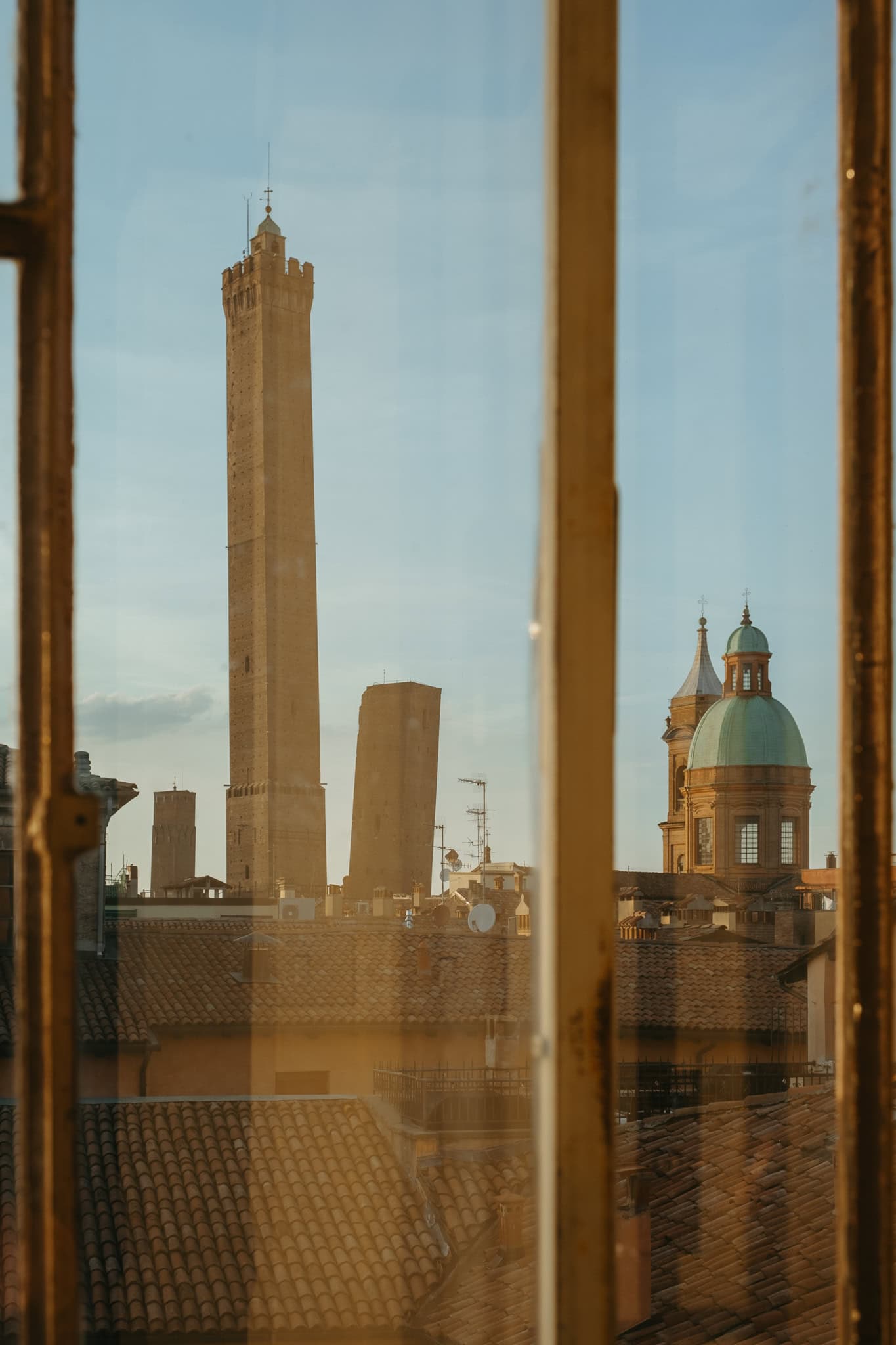 Two leaning towers and a church are seen through a window.