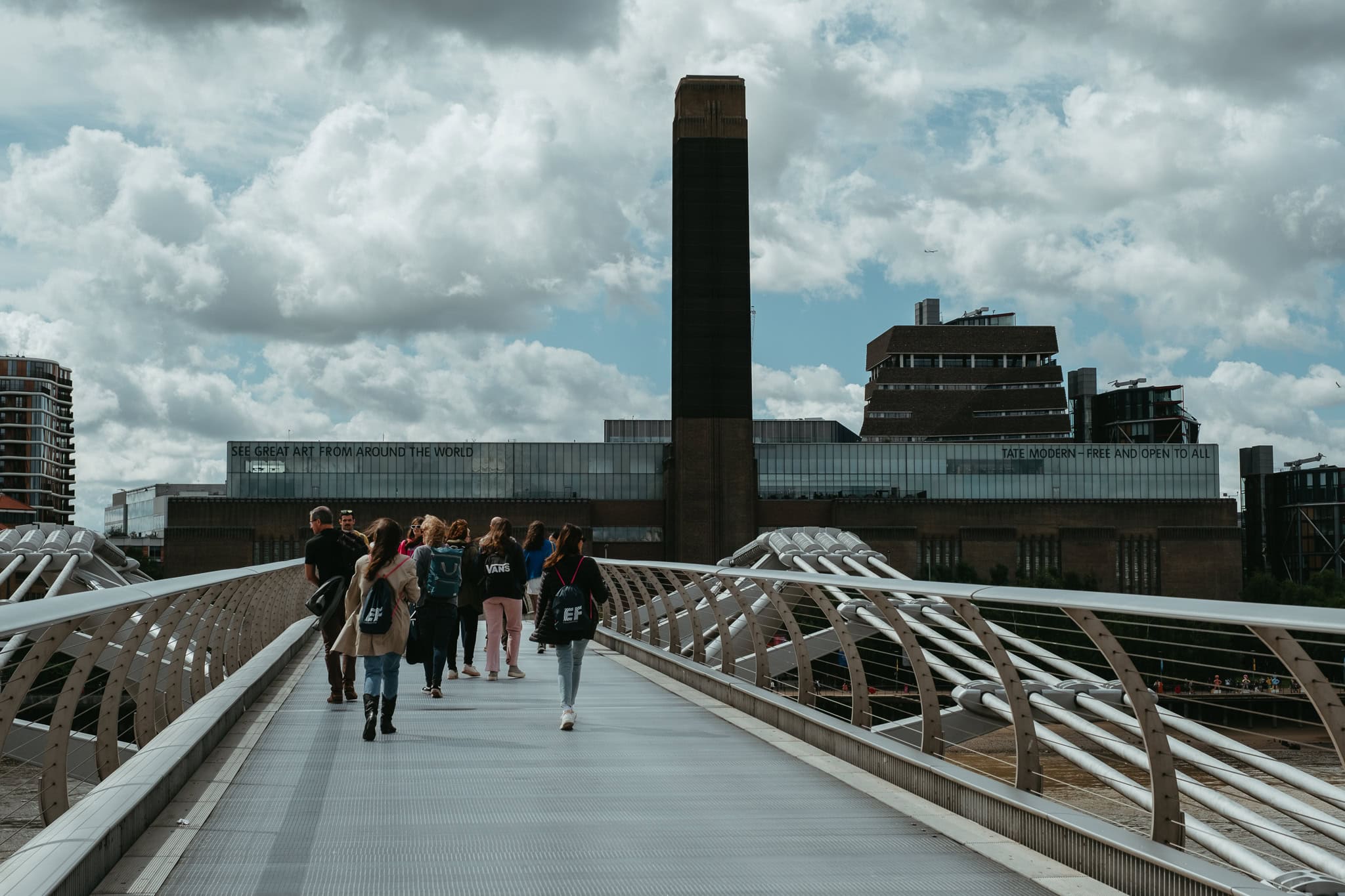 People walk across a pedestrian bridge in front of a large museum.