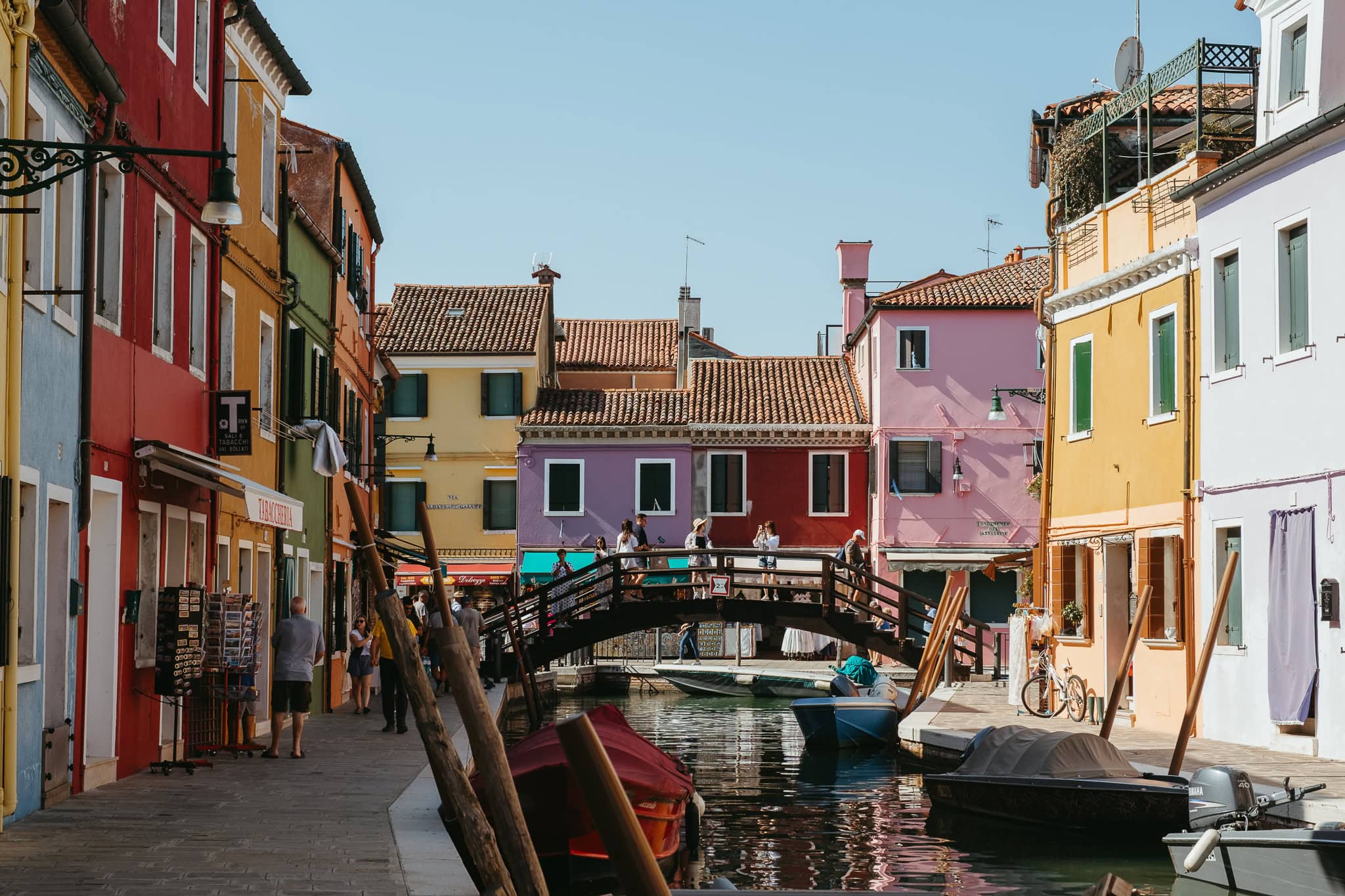 People walk over a bridge in front of brightly colored houses.