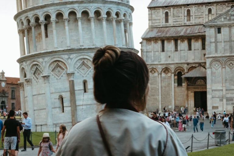 The back of a woman's head as she looks toward the Leaning Tower of Pisa and Pisa Cathedral.