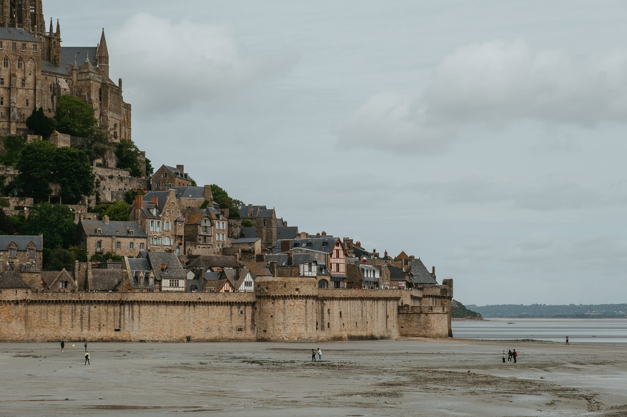 People walking on the sands outside the walls of Mont St. Michel.
