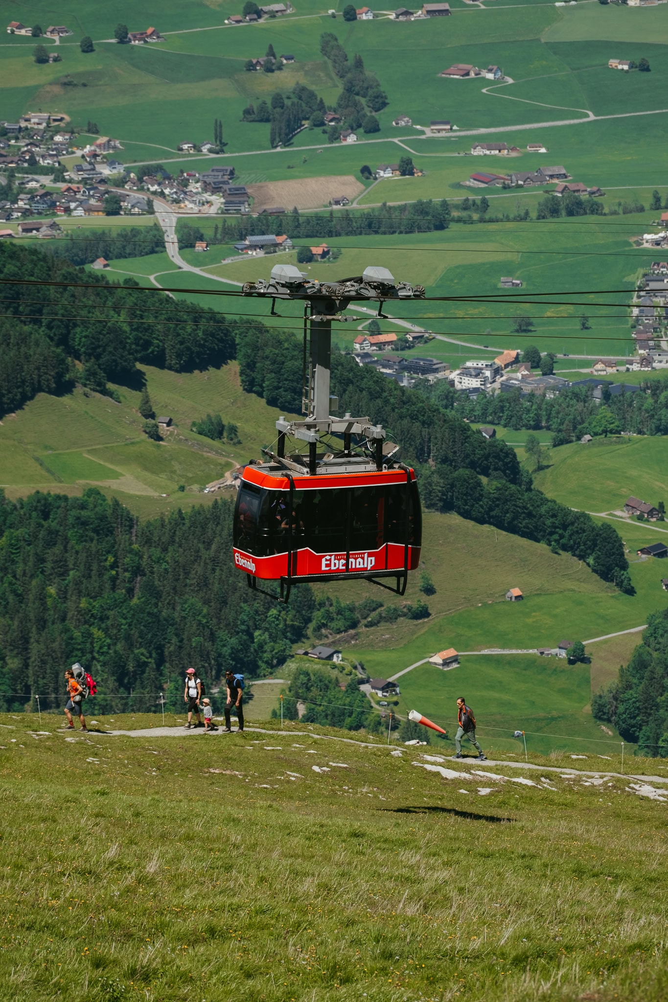 A red cable car that says "Ebenalp" above hikers.