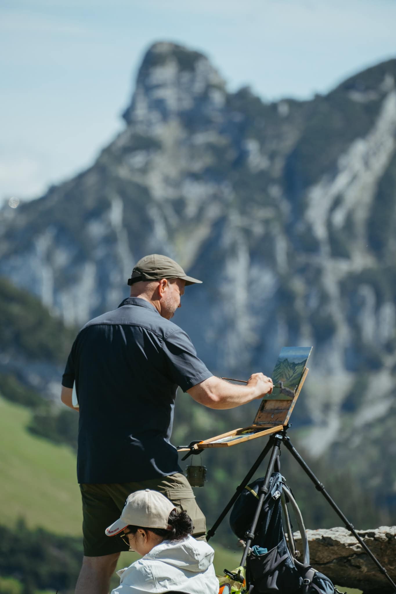 Person painting at an easel in front of a mountain.