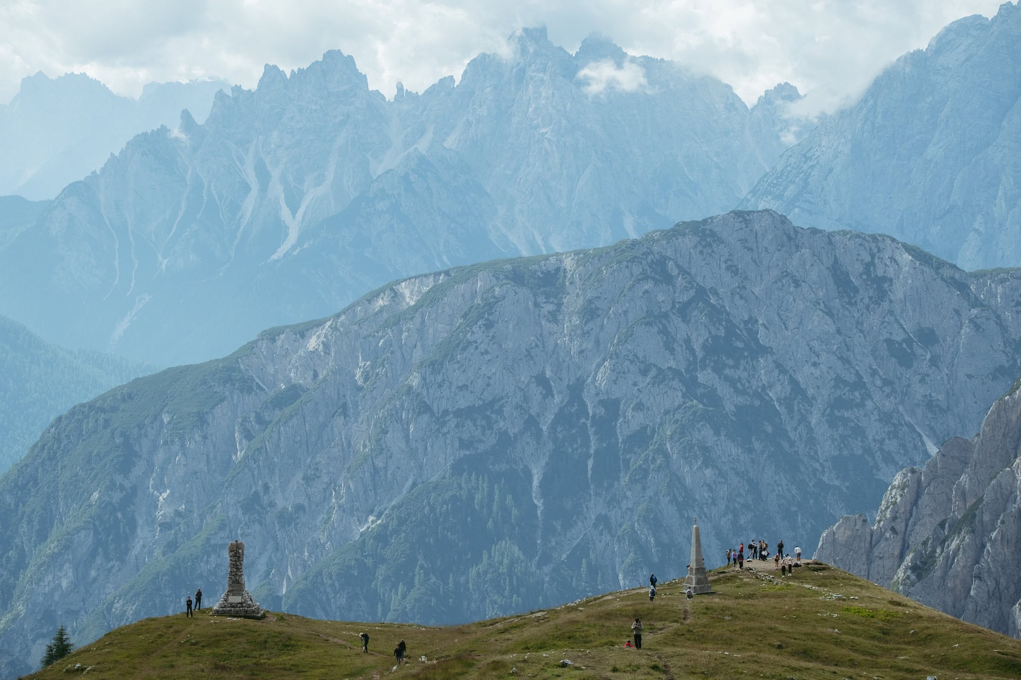 People standing at hilltop viewpoints in front of huge mountains.