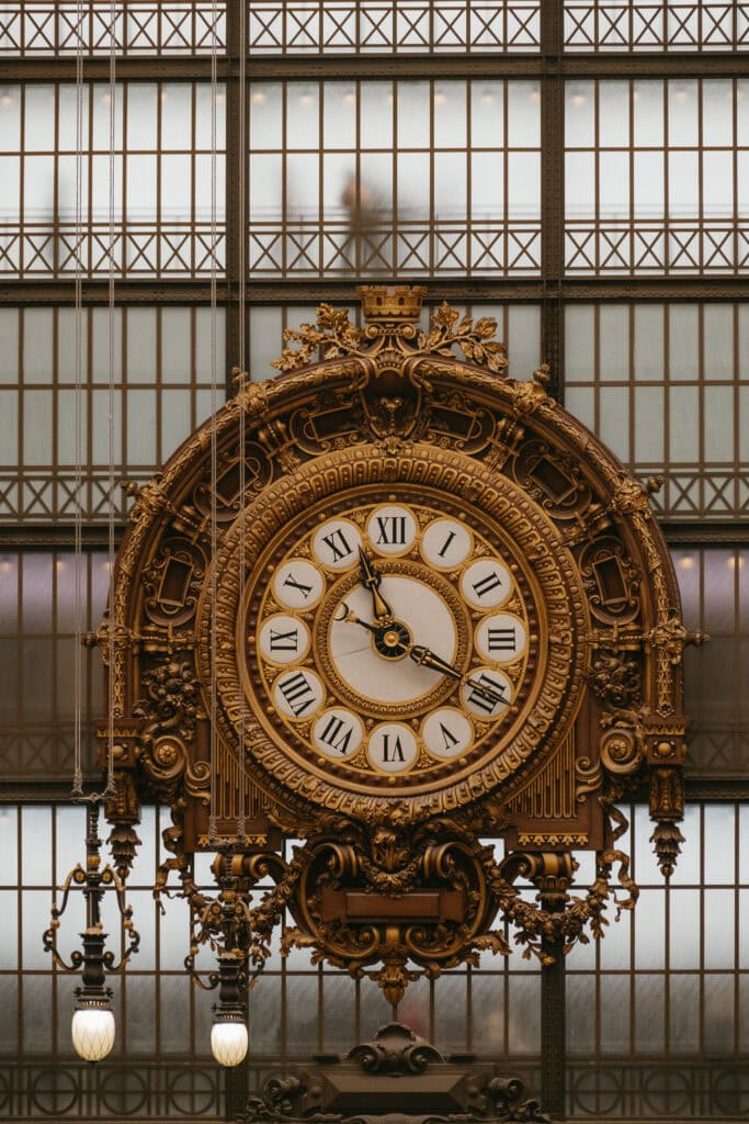 An ornate clock hanging in front of a glass wall.