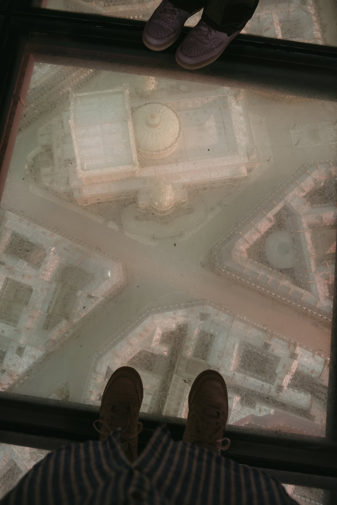 Feet standing on top of a glass floor with a model of the streets of Paris underneath.