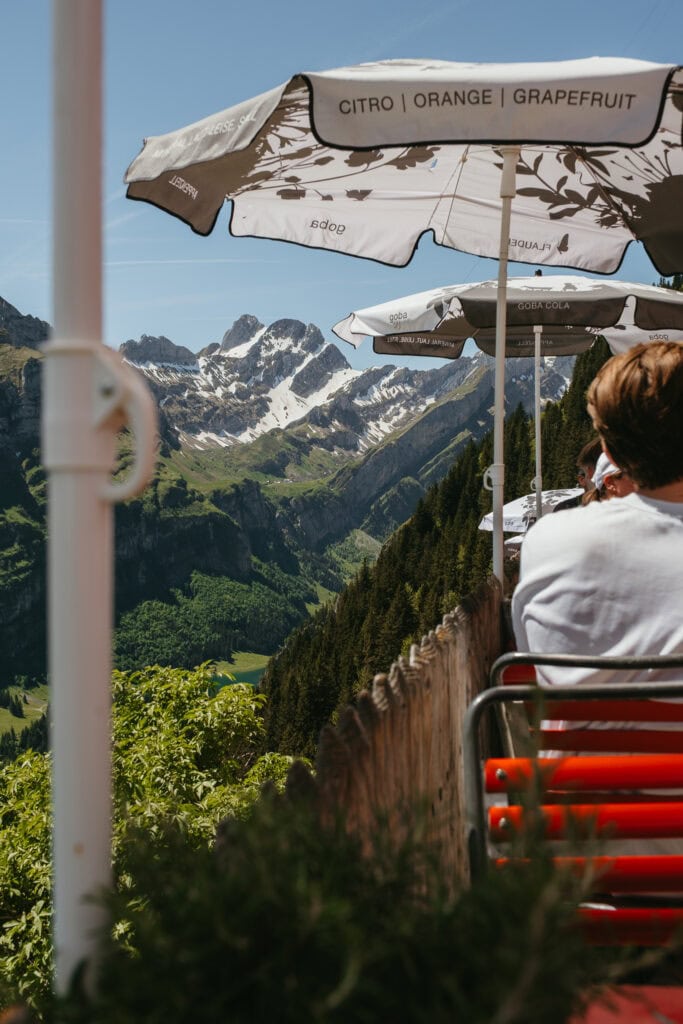 Tables at the edge of an outdoor restaurant terrace, with snow-capped mountains in the distance.