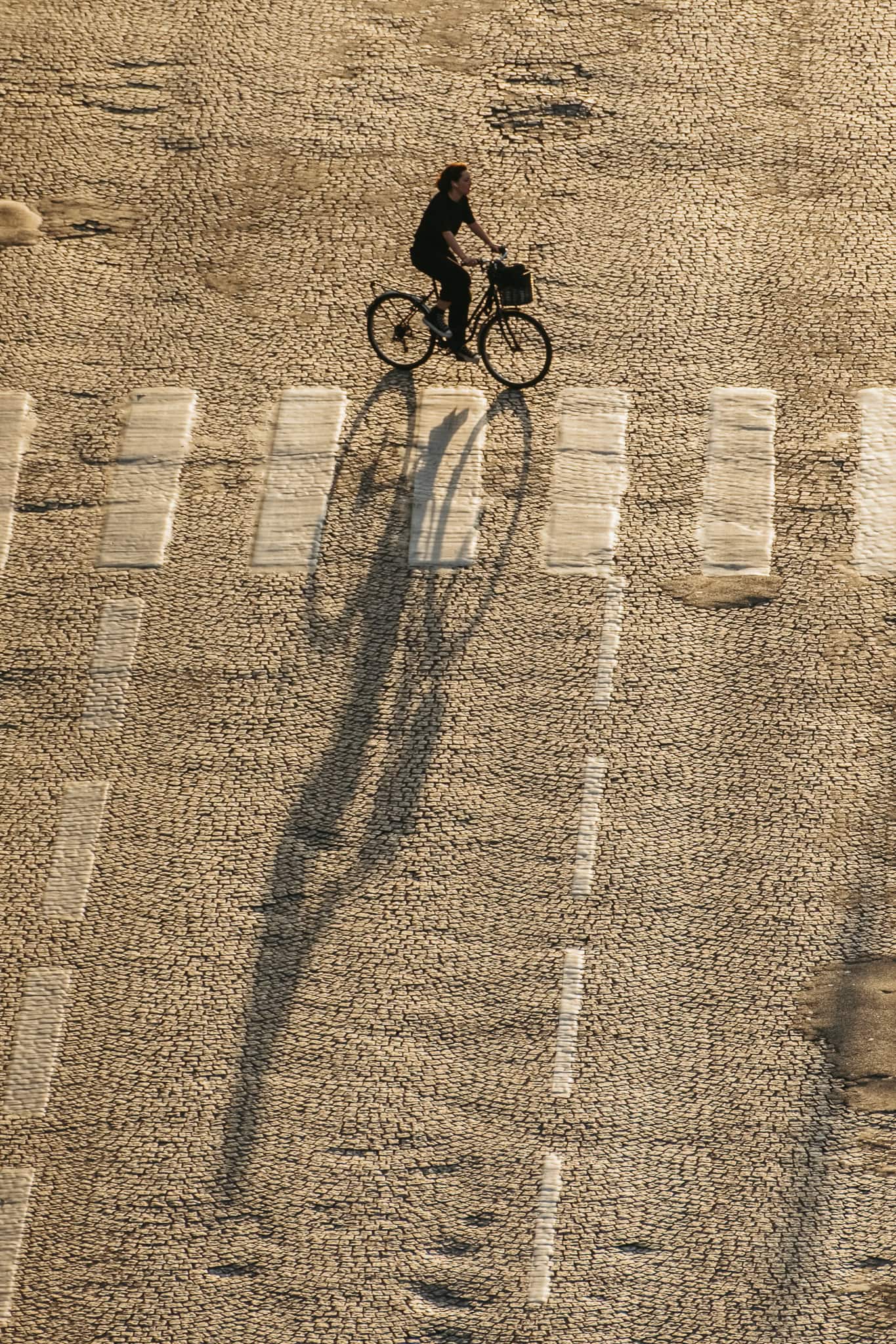 A bicyclist crossing the street with a long shadow.