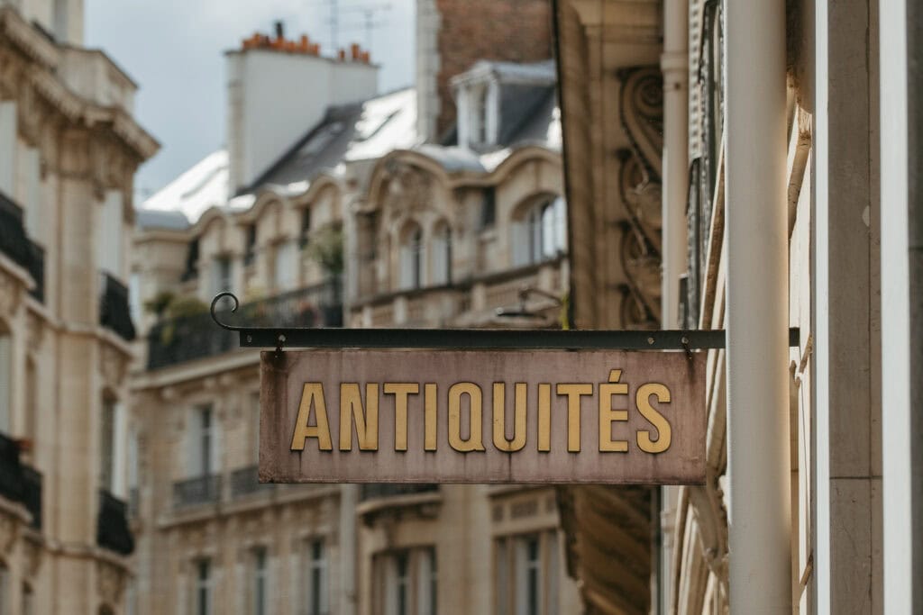 A sign stating "antiquites" hanging from the side of a building.