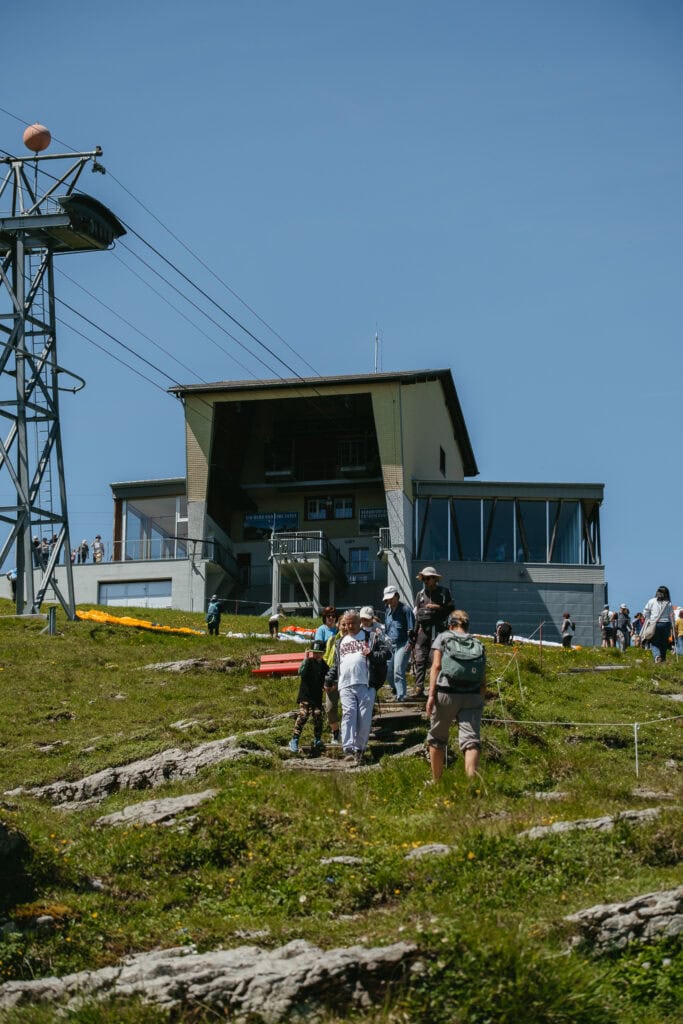 People hiking on a hill below a cable car station.