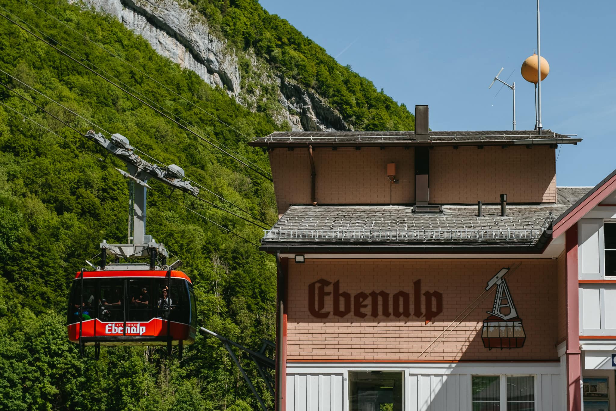 A cable car station that says "Ebenalp" with a red cable car gliding away.
