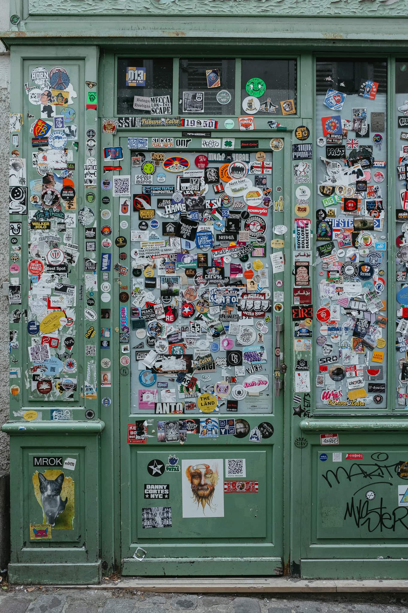 A green storefront with the windows covered in stickers.