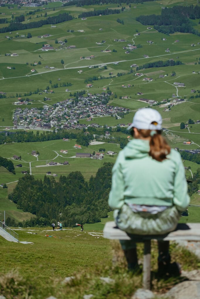 A woman sits on a hilltop with a town far in the valley below.
