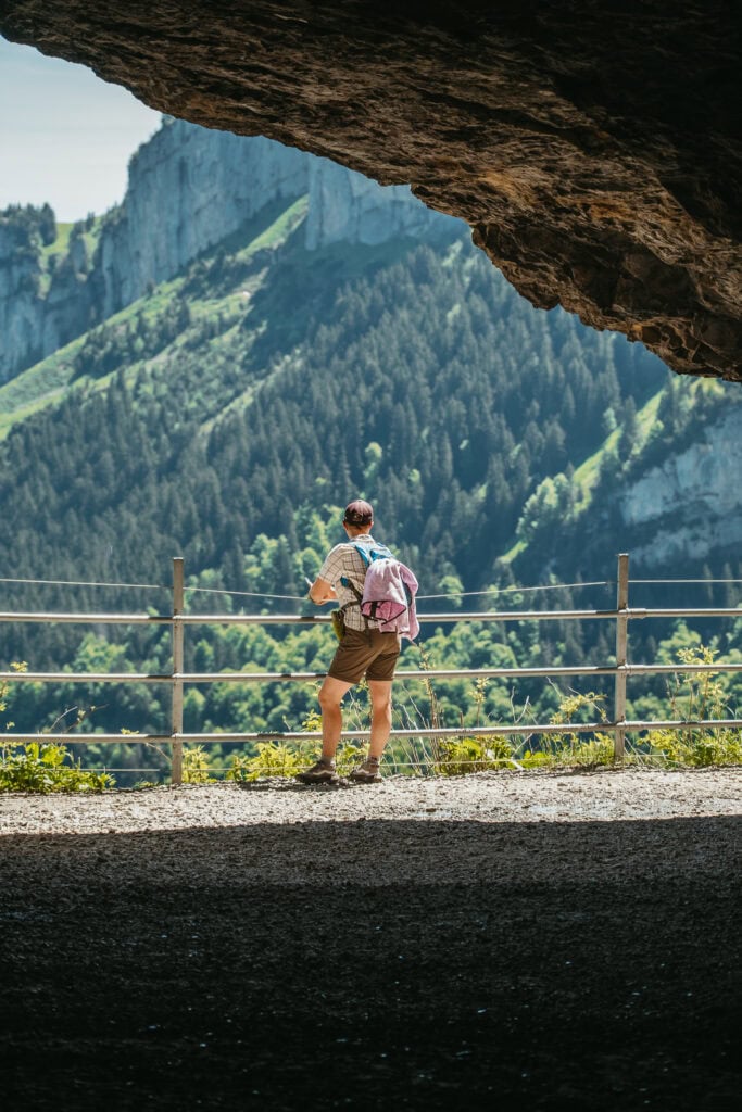 A person stands at a railing in front of a cave.