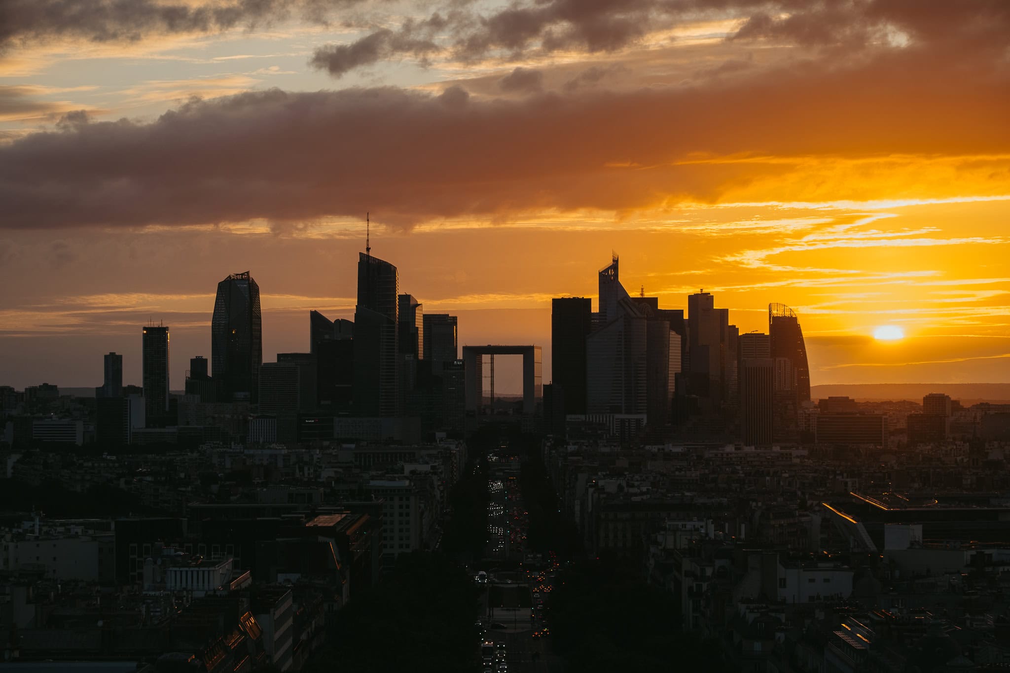 The sun sets beside a group of skyscrapers.