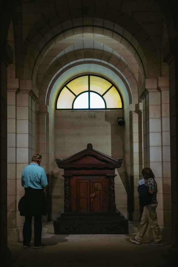 People looking at a tomb under stained glass windows.