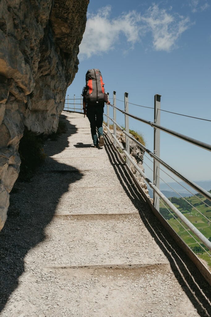 A hiker walking up a cliffside path with a railing.